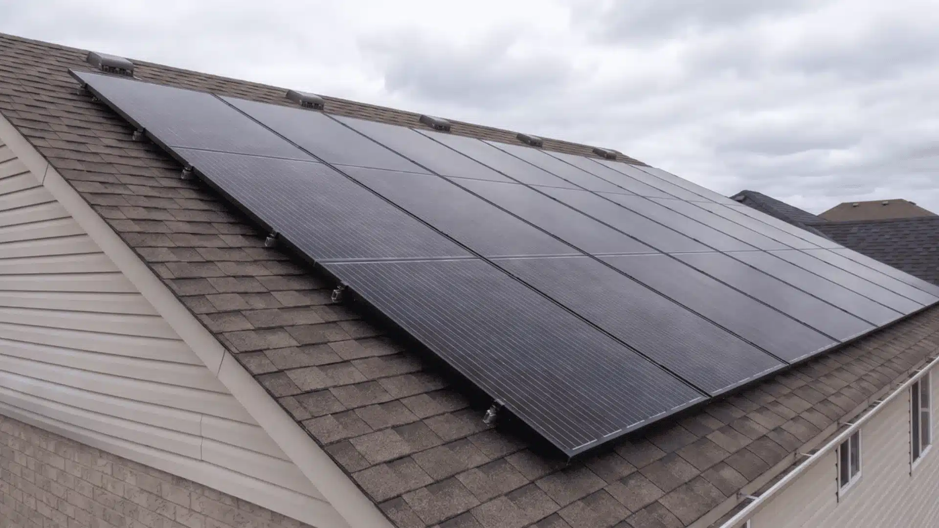 Solar panels mounted on a sloped residential roof beneath a cloudy sky.