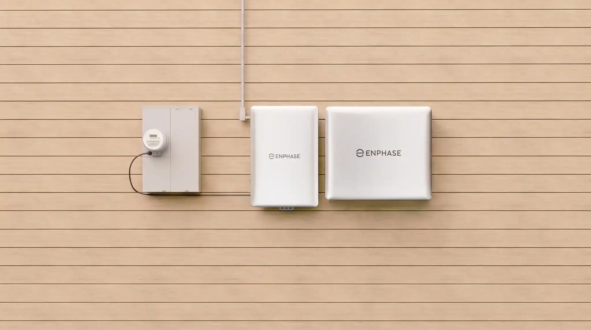 Wall-mounted Enphase home energy system with meter box, inverter and two battery units on wooden exterior siding.