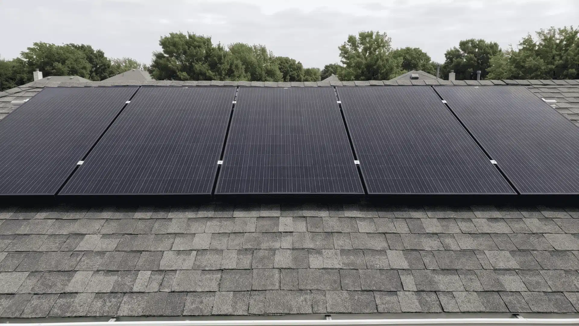 Solar panels on residential roof with neighborhood and trees in background