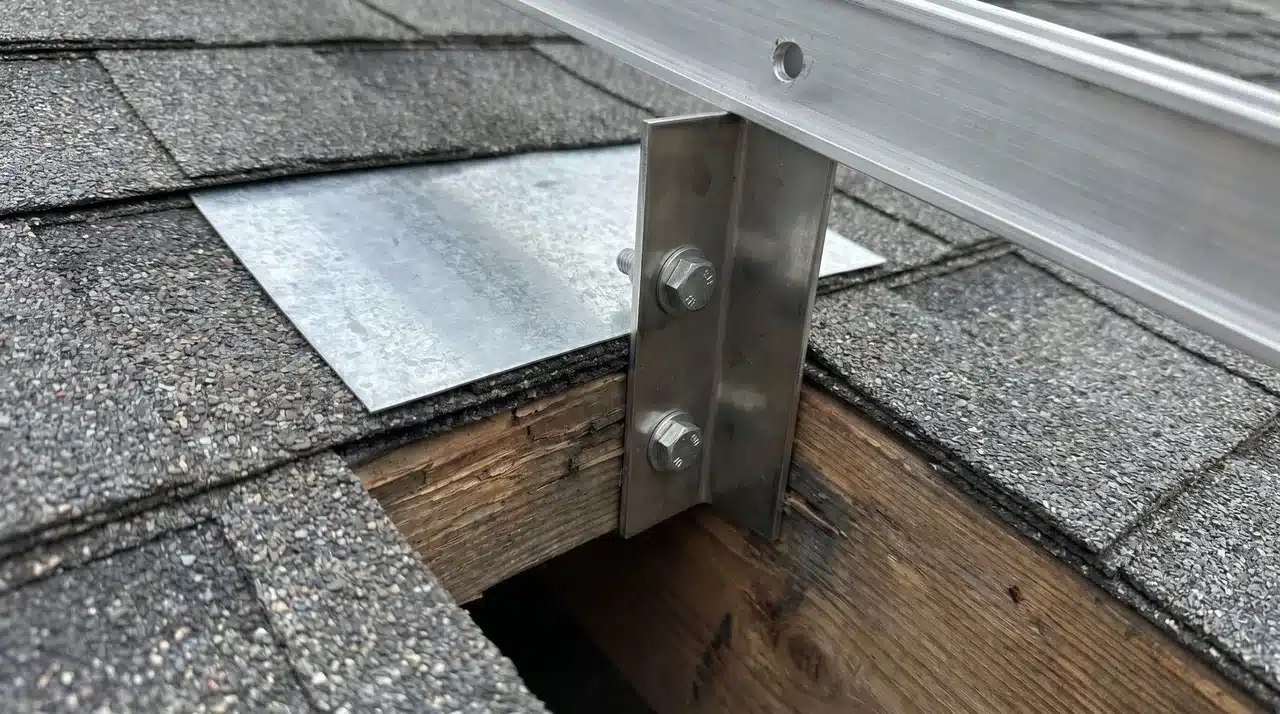 Stainless steel mounting bracket bolted through asphalt shingles with metal flashing tucked beneath surrounding shingle edges
