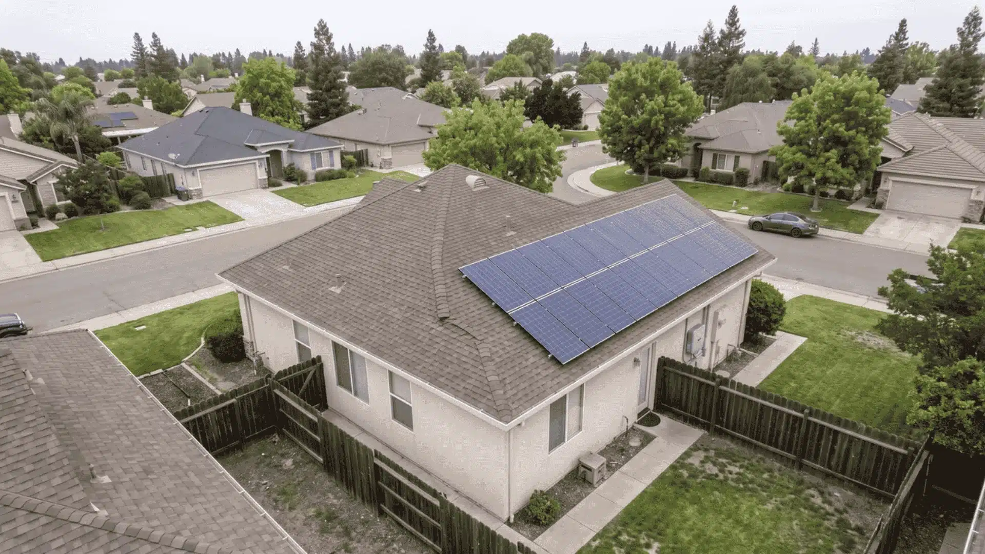 Solar panels installed on a residential rooftop viewed above a suburban neighborhood.