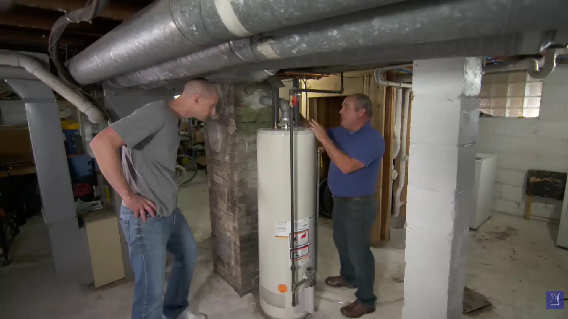 Two men inspect a water heater and exposed ductwork inside an unfinished home basement