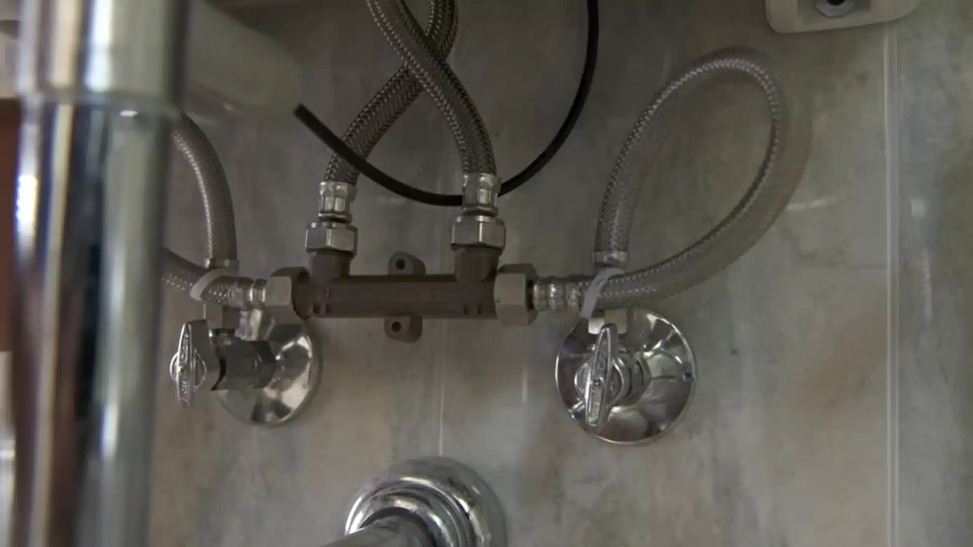 Braided supply hoses connect a hot-water recirculation valve beneath a bathroom sink