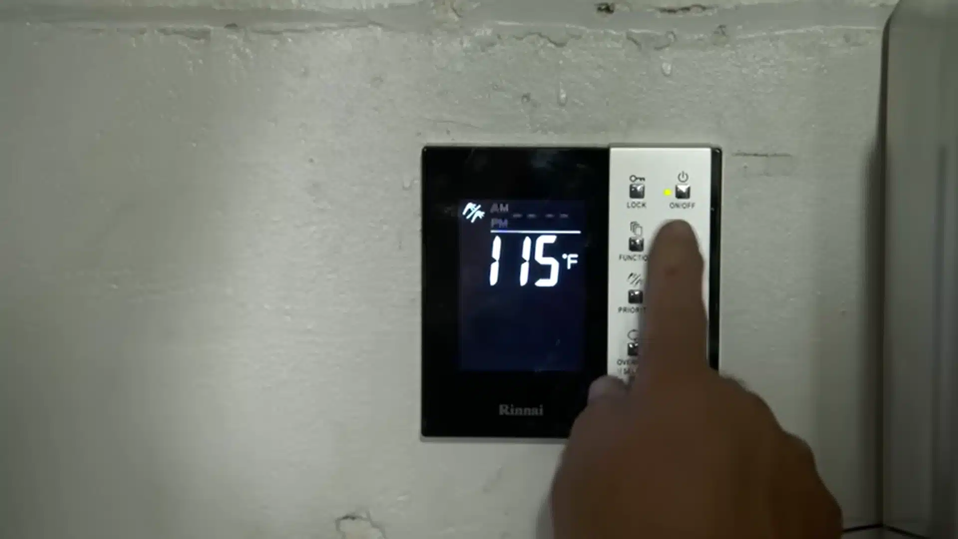Hand adjusts a tankless water heater control panel set to 115 degrees Fahrenheit