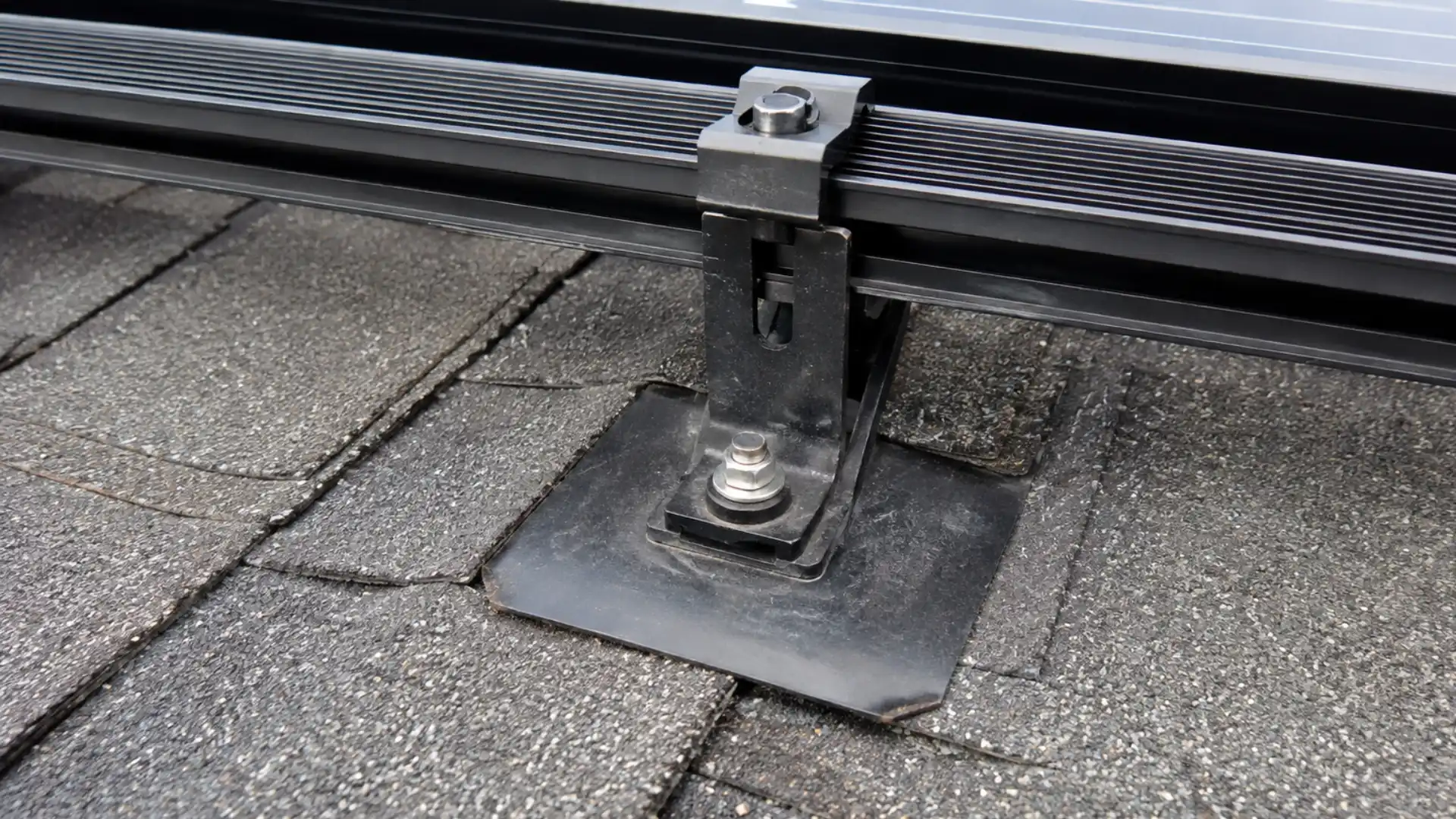 Close up of a solar panel mounting bracket bolted through asphalt shingles into decking