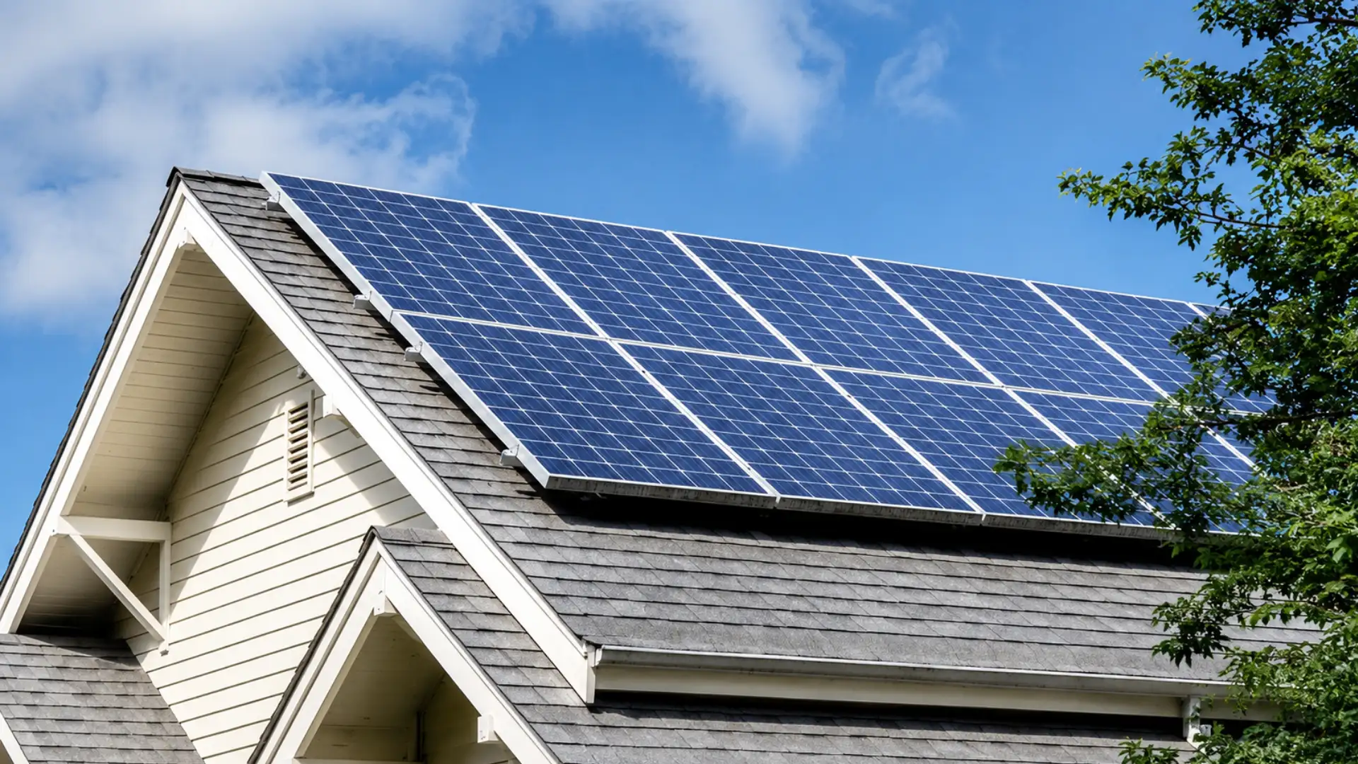 Blue solar panels installed on a gray shingle house roof beneath a bright clear sky