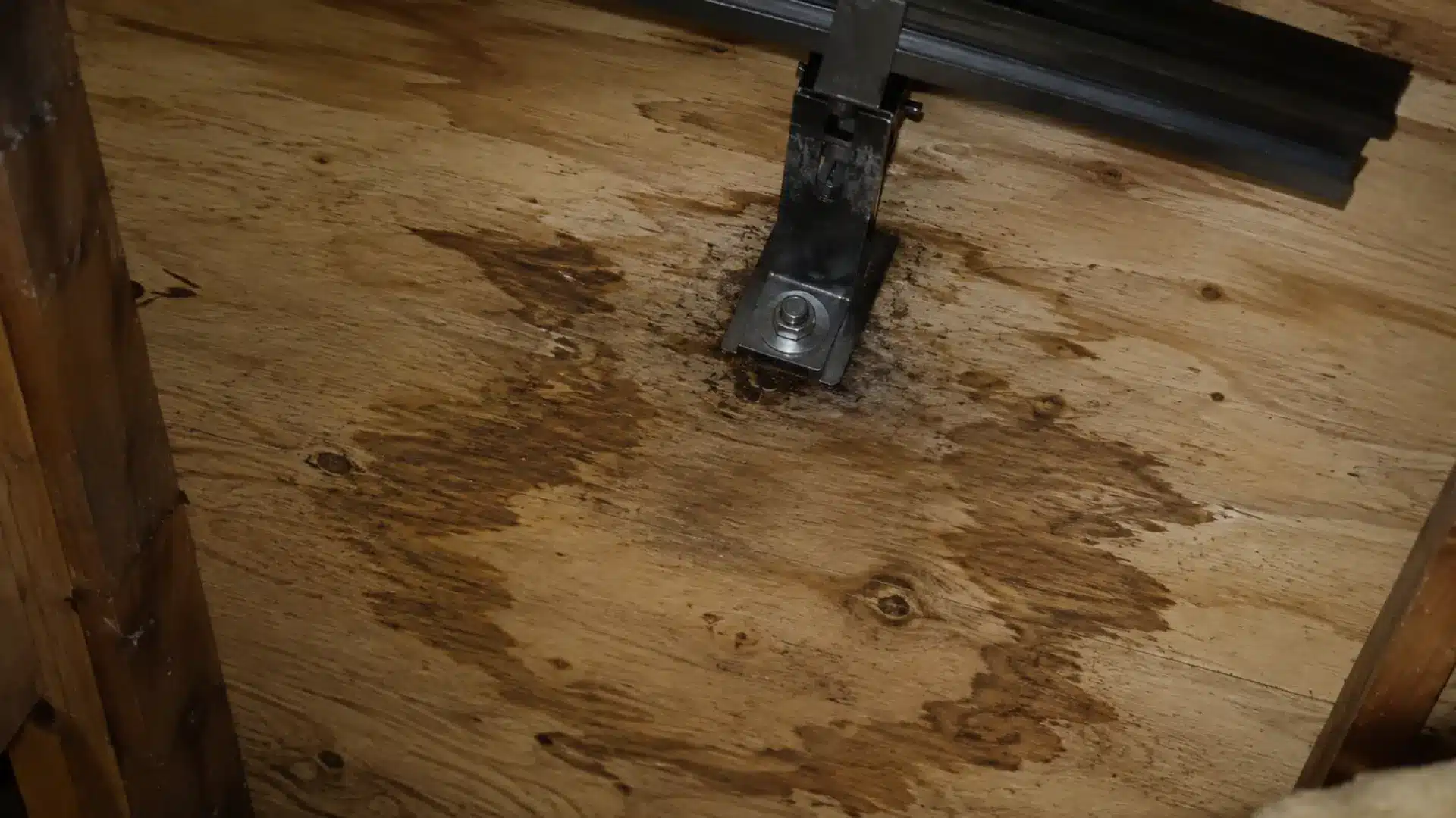Water stain spreading across plywood roof decking near a solar panel mounting bracket