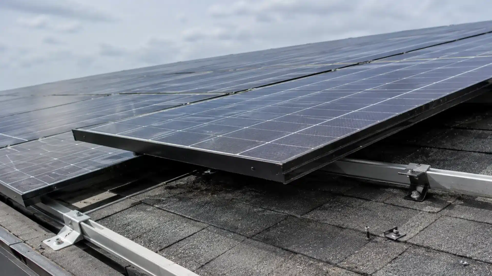 Solar panels partially lifted off mounting rails exposing bare shingles underneath