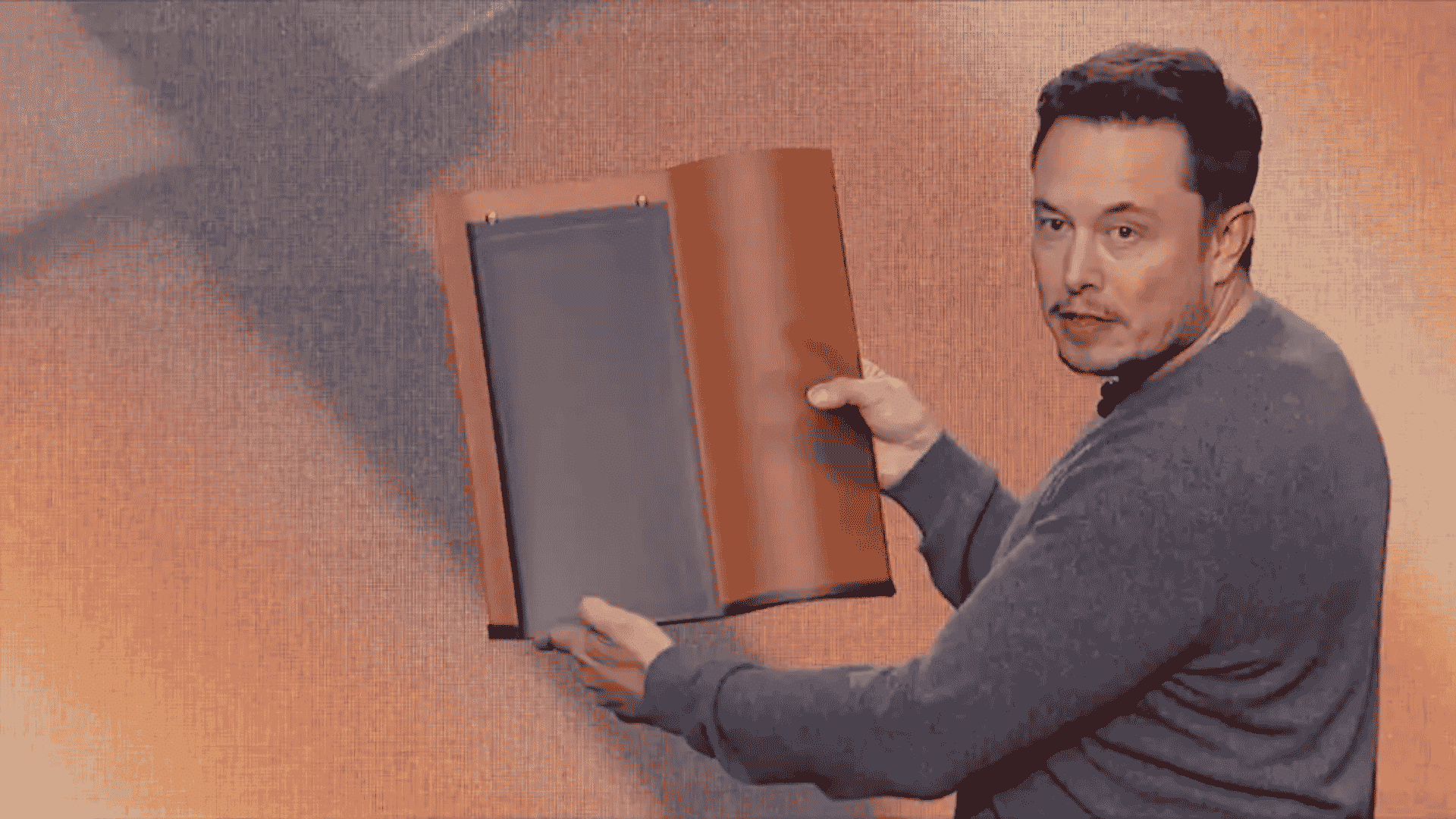 Elon Musk holding up a Tesla Solar Roof tile prototype on stage during a product presentation.