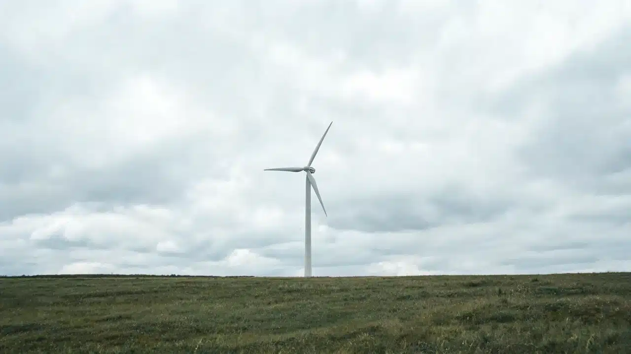 A single wind turbine standing alone in a wide grassy field under a heavily overcast dramatic cloudy sky